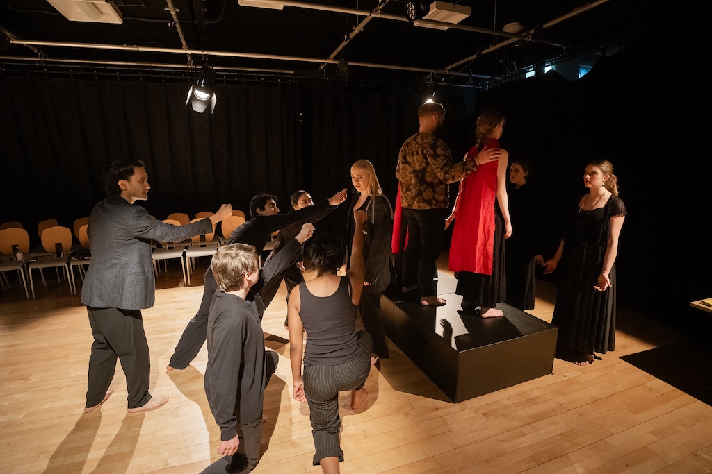 Group of actors, two standing on a black riser while the others are standing or kneeling below them, during the final presentation of The Winter's Tale.